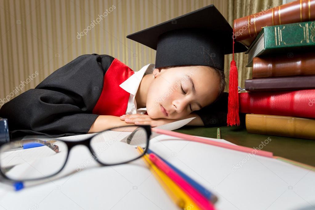 Portrait of tired girl in graduation cap seeping at library