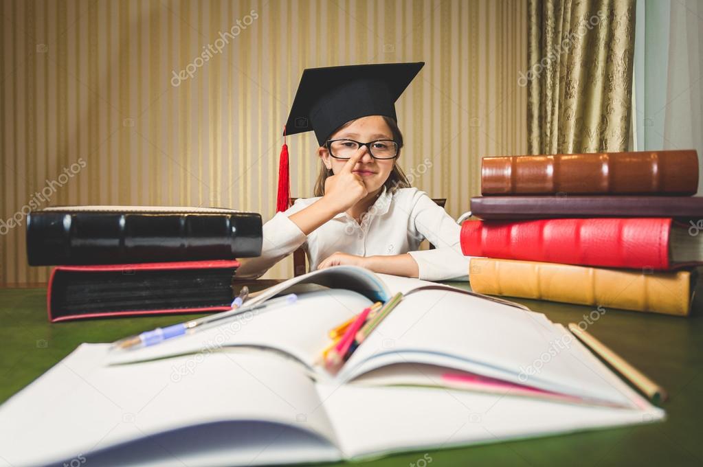 girl wearing eyeglasses and graduation cap posing at desk