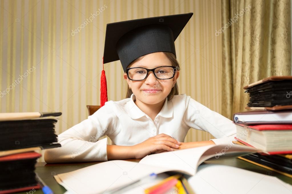 portrait of smiling little girl in graduation hat sitting at tab