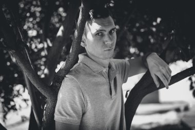 Kendine güvenen delikanlı ağaca yaslanmış siyah beyaz portre