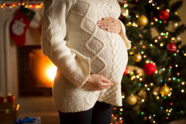 Gravid kvinna poserar mot öppen spis och julgran — Stockfoto
