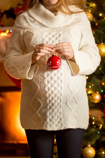 Pregnant woman posing against fireplace with Christmas ball — Stock Photo, Image