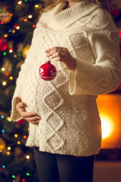 Pregnant woman in wool sweater holding red Christmas ball — Stock Photo, Image