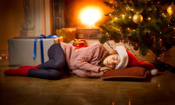 Κορίτσι που κοιμούνται στο πάτωμα κάτω από το χριστουγεννιάτικο δέντρο δίπλα στο τζάκι — Φωτογραφία Αρχείου
