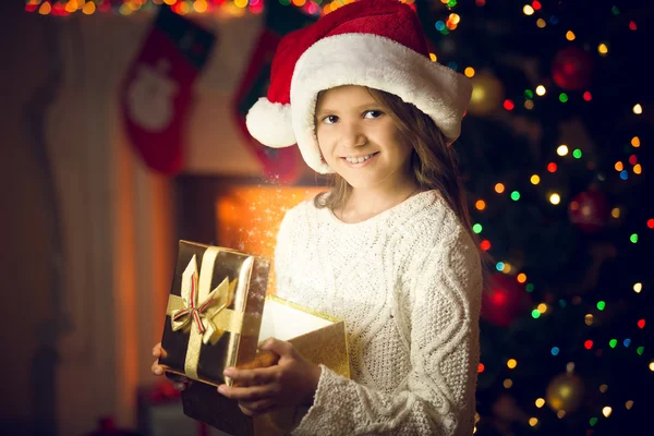 Porträt eines lächelnden Mädchens mit Weihnachtsmannmütze, das mit glühenden Geschenken posiert — Stockfoto