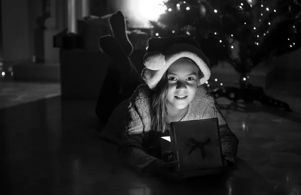 Chica sonriente acostada con caja de regalo de Navidad en el suelo junto al fuego —  Fotos de Stock