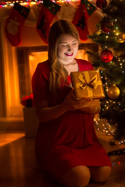 Glad ung kvinna titta inuti jul presentförpackning på natten — Stockfoto