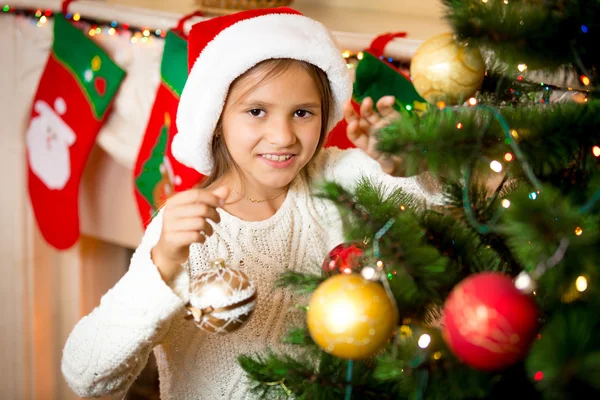 Süßes lächelndes Mädchen schmückt Weihnachtsbaum mit goldenen Kugeln — Stockfoto