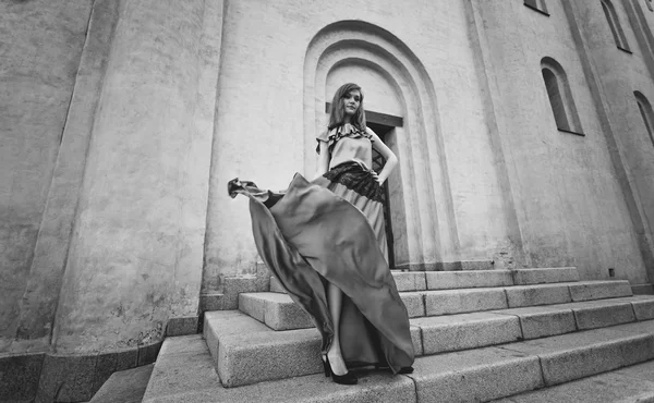 Beautiful woman in long dress posing on stairs at windy day — Stock Photo, Image