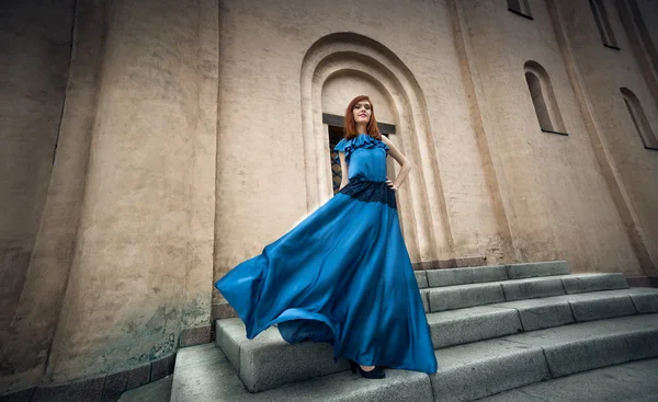 Frau im flatternden langen blauen Kleid, die auf Steintreppe posiert — Stockfoto