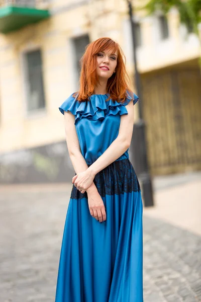 Elegante rothaarige Frau im langen blauen Kleid posiert auf der alten Straße — Stockfoto