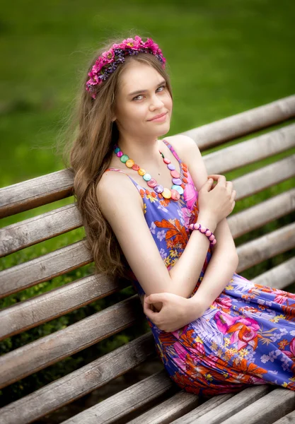 Mooie vrouw in jurk ontspannen op houten bankje in het park — Stockfoto