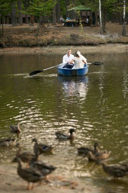 newly married couple riding on rowing boat on lake at forest clipart
