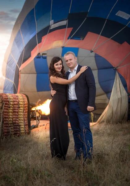 Romantic couple hugging against hot air balloon at meadow — Stock Photo, Image