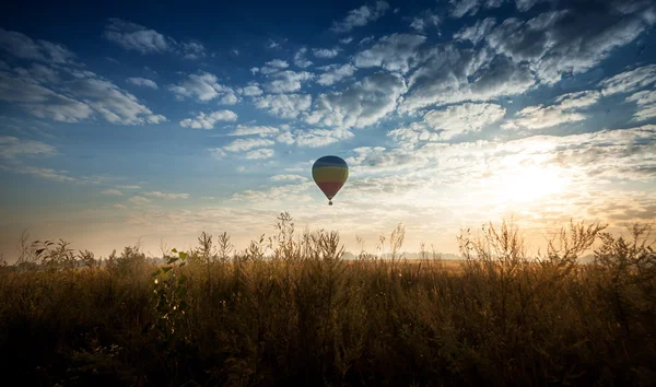Weergave van de luchtballon vliegt over het veld bij zonsopgang — Stockfoto