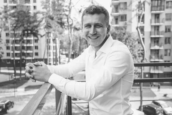 Elegante uomo sorridente in camicia bianca in posa sul balcone contro urb — Foto Stock