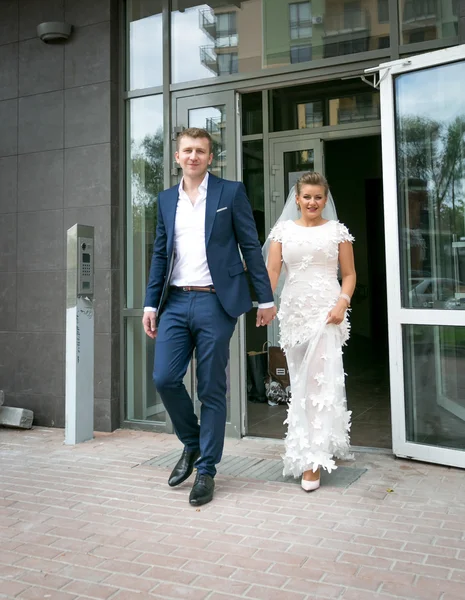 Happy bride and groom walking out of modern building — Stock Photo, Image