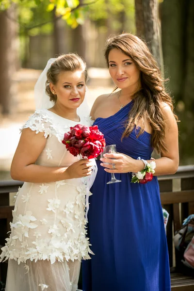 Mariée heureuse et demoiselle d'honneur posant au parc — Photo