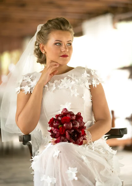 Portrait of beautiful elegant bride with red bouquet siting on c — Stock Photo, Image