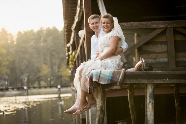 Happy bride and groom relaxing on wooden pier on lake at forest — Stock Photo, Image