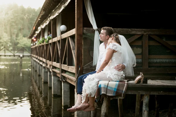 Novia y el novio sentado en el muelle y mirando al río y para — Foto de Stock