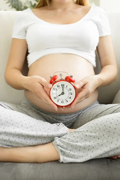 Terhes nő pózol a piros ébresztőóra a kanapé — Stock Fotó