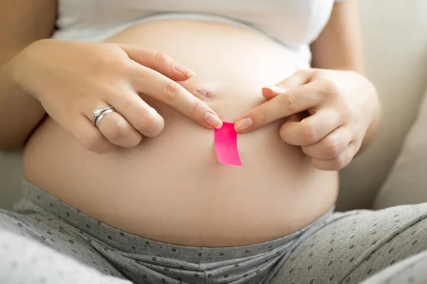 Mulher grávida colando adesivo memorando rosa na barriga — Fotografia de Stock