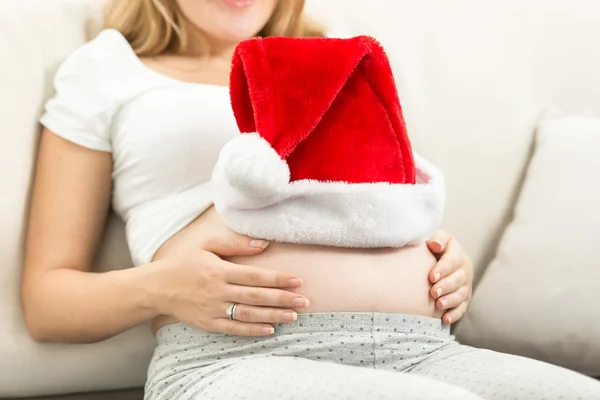 Closeup of red Santa cap on pregnant woman belly — Stock Photo, Image