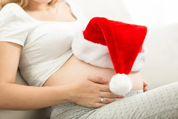 Closeup of pregnant woman holding Santa cap on tummy — Stock Photo, Image