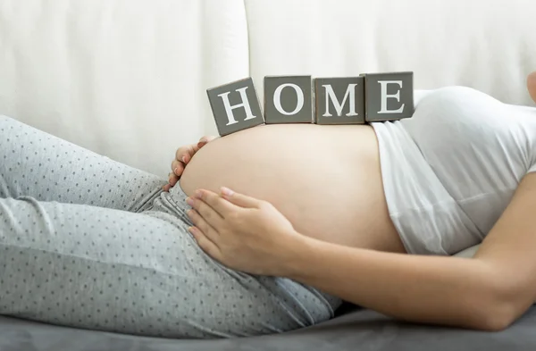 Closeup of pregnant woman holding word Home on belly — Stock Photo, Image