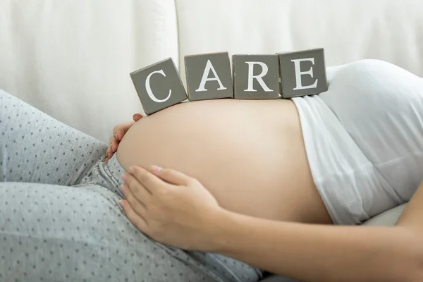 Letters on blocks making word Care on pregnant women tummy — Stock Photo, Image