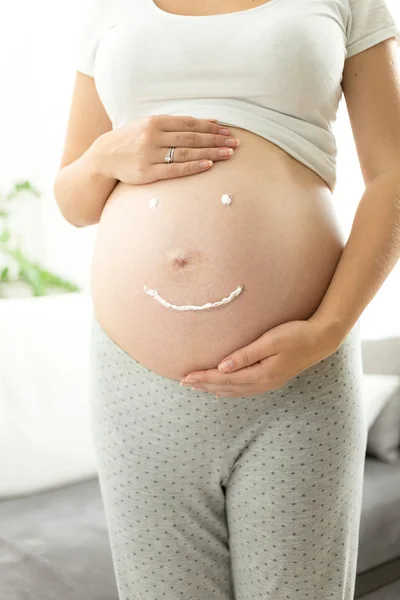 Closeup of smile drawn by creme on pregnant belly — Stock Photo, Image