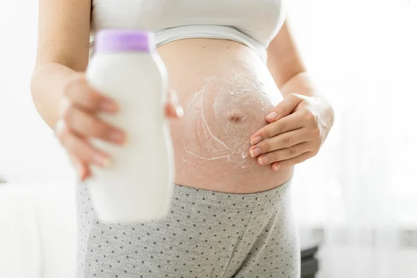 Closeup of pregnant woman applying creme and holding creme bottl — Stock Photo, Image