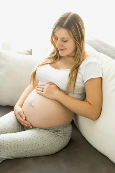 Gravid kvinna att koppla av på soffan och tittar på magen — Stockfoto