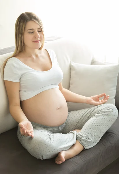 Donna incinta che pratica yoga sul divano in soggiorno — Foto Stock