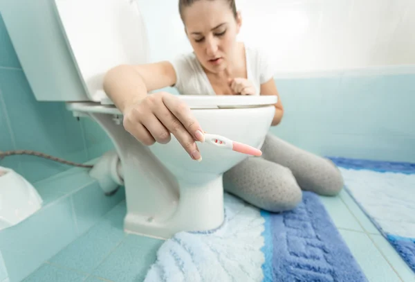 Chateado mulher segurando teste de gravidez positivo no banheiro — Fotografia de Stock
