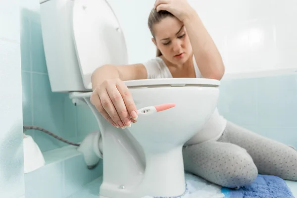 Sad sick woman sitting in bathroom and holding positive pregnanc — Stock Photo, Image