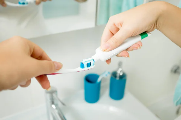 Primer plano de la mujer poniendo pasta de dientes en el cepillo de dientes en el baño —  Fotos de Stock