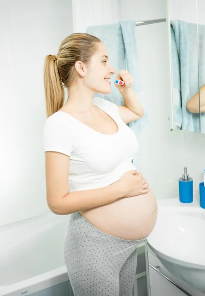 Beautiful pregnant woman brushing teeth at bathroom — Stock Photo, Image