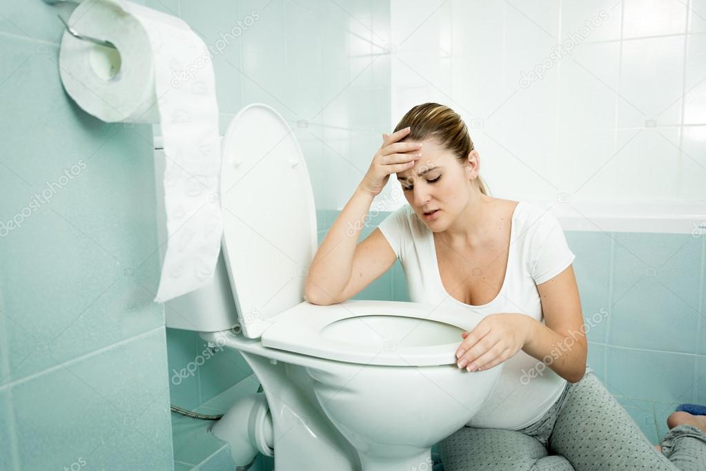 Pregnant woman leaning on toilet and feeling sick