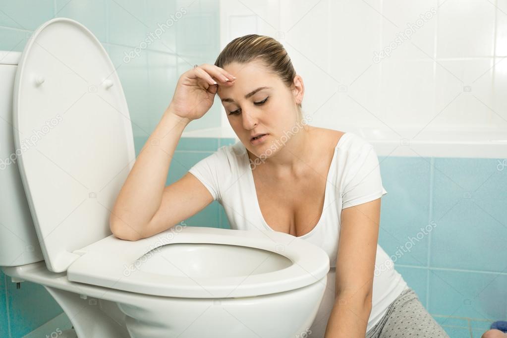 young woman feeling sick and leaning on toilet