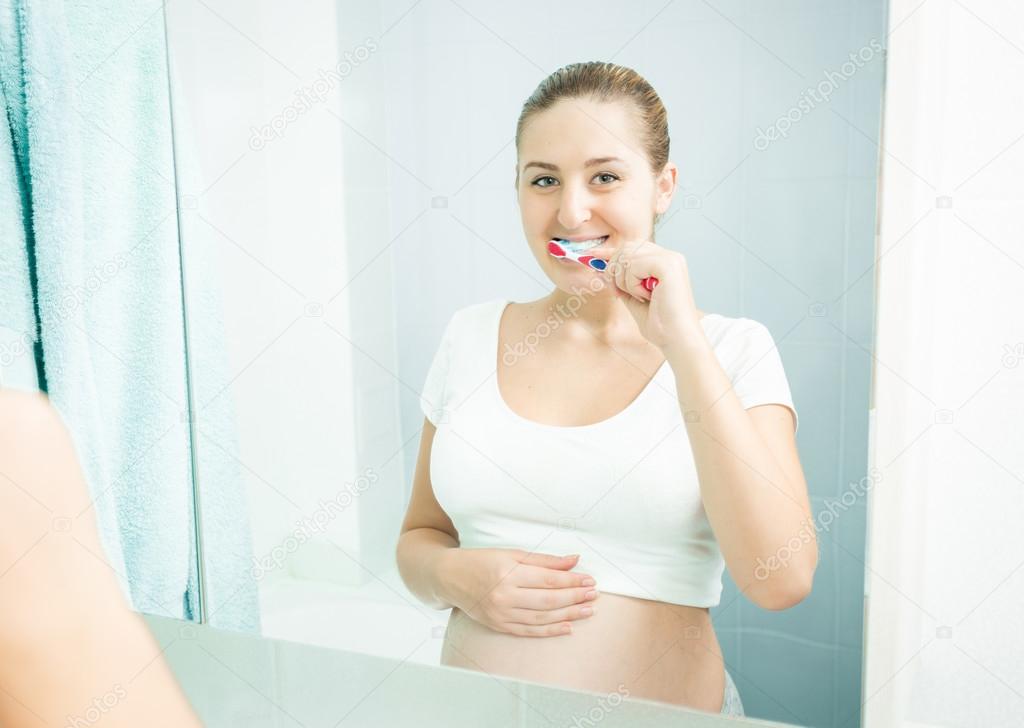 young pregnant woman brushing teeth at bathroom