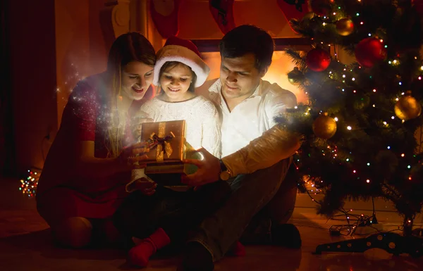 Lachende familie op zoek binnenkant van gloeiende doos van de gift van Kerstmis — Stockfoto