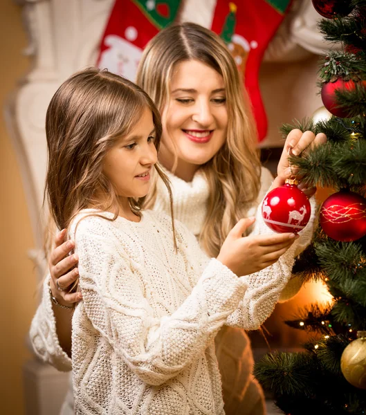 クリスマス ツリーを飾るために母親を助ける少女の笑みを浮かべてください。 — ストック写真