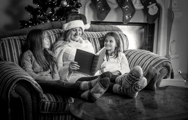 Retrato de la madre con dos hijas leyendo libro en el sofá en abeto — Foto de Stock