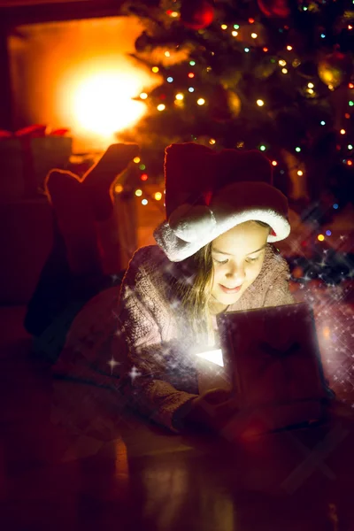 女孩躺在圣诞树下，看上去在闪闪发光礼品博 — 图库照片