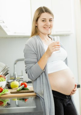 gülümseyen kadın bekliyor bebek mutfak wat bardak ile poz