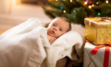Yeni doğan bebek çocuk Noel ağacının yanındaki battaniyenin altında yalan ve 