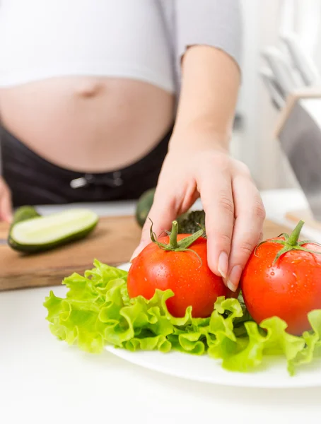 Nahaufnahme einer schwangeren Frau, die frische Tomaten vom Teller nimmt — Stockfoto