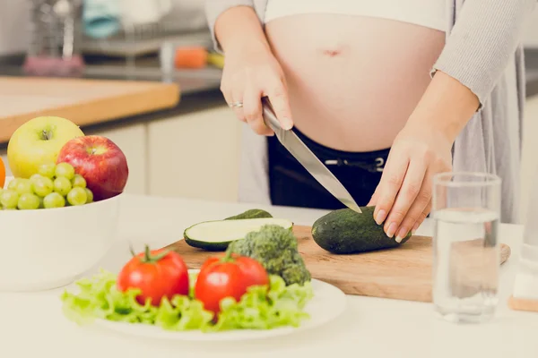 Тонированное фото беременной женщины, делающей салат на кухне — стоковое фото